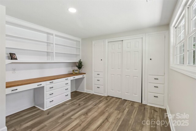 unfurnished office with built in study area, wood finished floors, baseboards, and recessed lighting