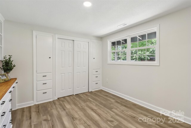 unfurnished bedroom with light wood-style flooring, baseboards, and a closet