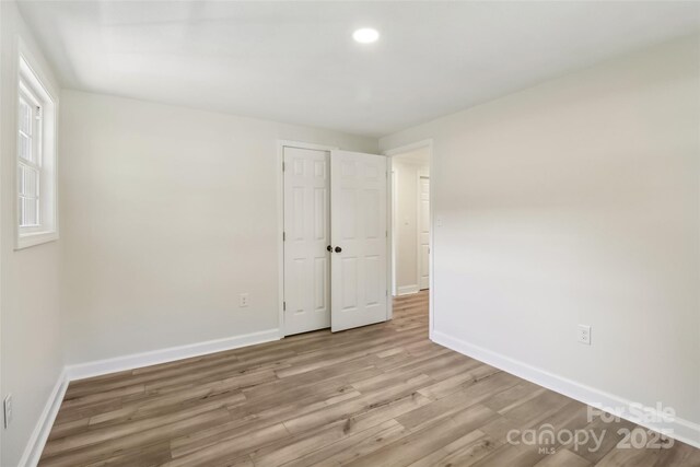 unfurnished bedroom featuring wood finished floors, baseboards, recessed lighting, and a closet