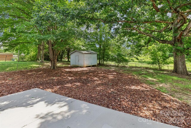 view of yard featuring a patio, a storage shed, an outbuilding, fence, and view of scattered trees
