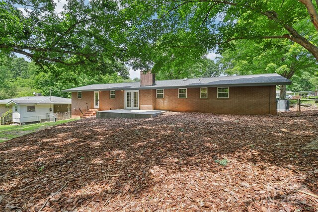 rear view of property with french doors, a chimney, and brick siding