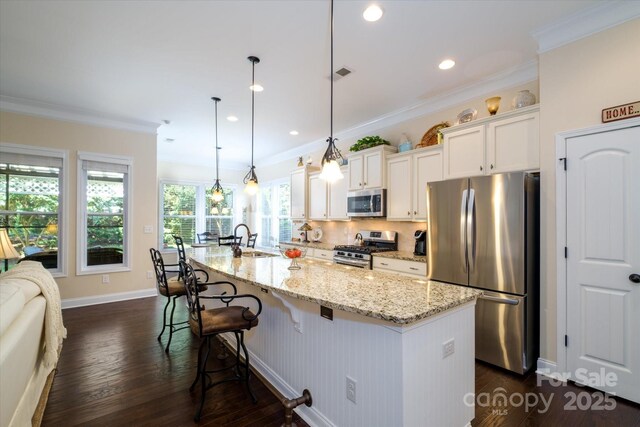 8818 Artesa Mill Ln, Charlotte, NC 28214 - kitchen with stainless steel appliances, a kitchen breakfast bar, a center island with sink, ornamental molding, and white cabinetry