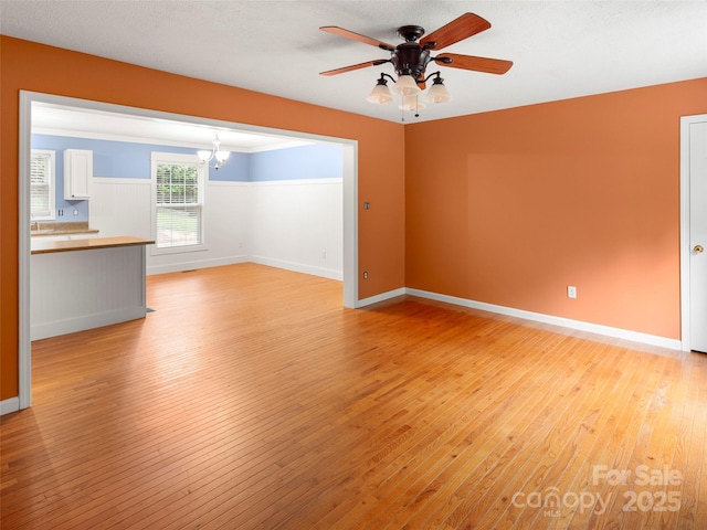 unfurnished room featuring light wood-type flooring, a chandelier, a ceiling fan, and baseboards