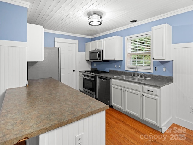 kitchen featuring stainless steel appliances, a sink, dark countertops, white cabinetry, and a wainscoted wall