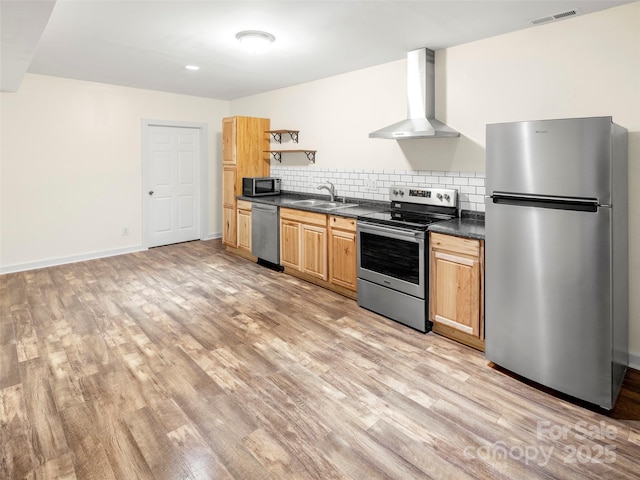 kitchen featuring stainless steel appliances, wall chimney range hood, dark countertops, a sink, and light wood-style floors