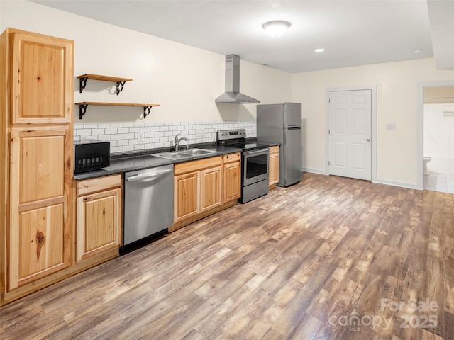 kitchen featuring appliances with stainless steel finishes, wall chimney range hood, a sink, dark countertops, and tasteful backsplash