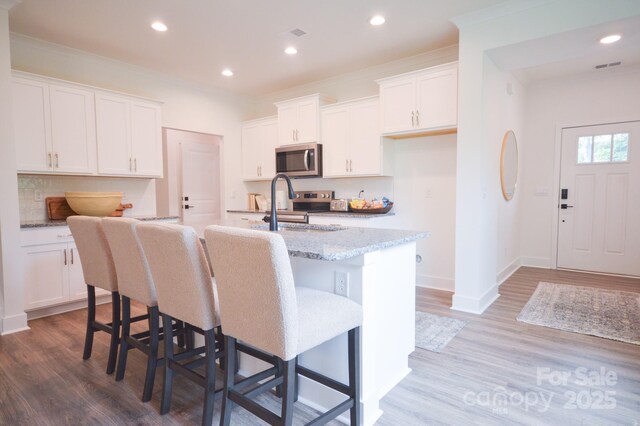 106 Sugg Trl, Weaverville, NC 28787 - kitchen featuring stainless steel microwave, a center island with sink, wood finished floors, white cabinets, and recessed lighting