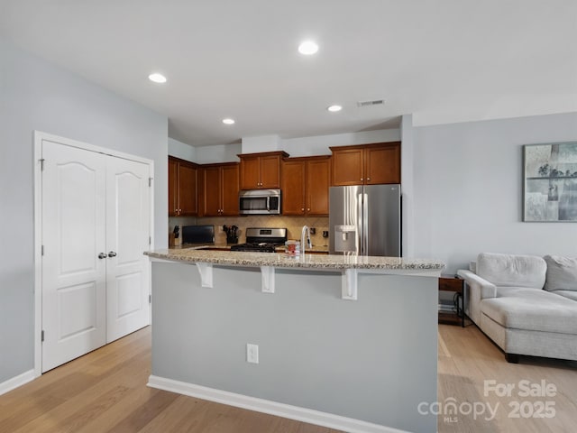 3306 Yarmouth Ln, Gastonia, NC 28056 - kitchen featuring stainless steel appliances, light stone counters, a kitchen breakfast bar, light wood-type flooring, and backsplash