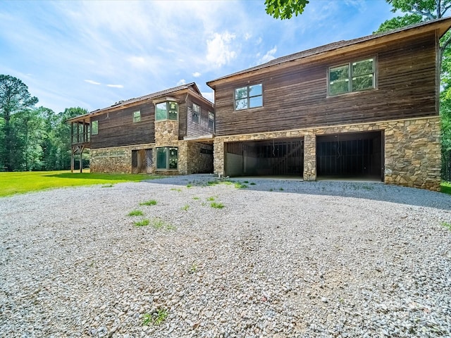 view of front of home with gravel driveway, stone siding, and an attached garage