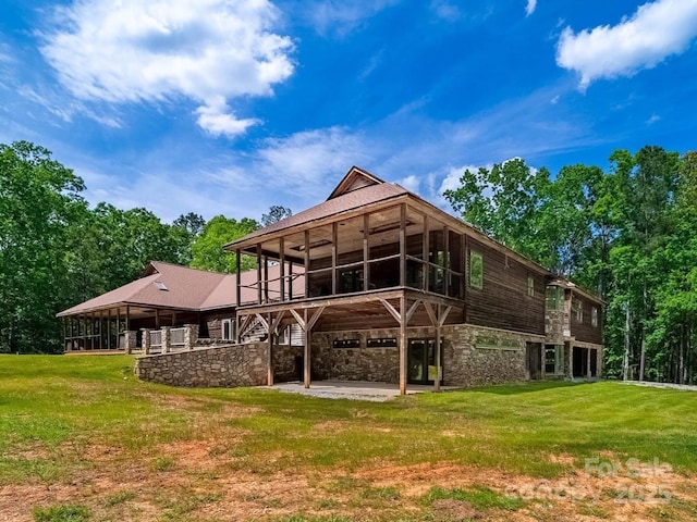 back of property with stone siding, a patio area, a sunroom, and a yard