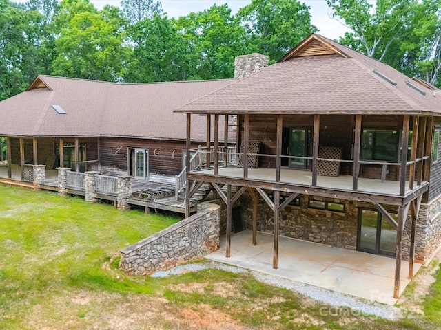 rear view of property featuring a chimney, a shingled roof, a patio area, a yard, and stone siding
