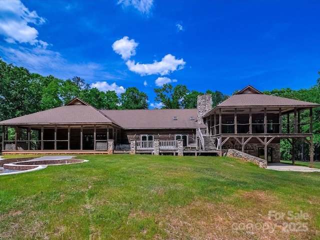 rear view of property featuring a sunroom, a chimney, a lawn, and a wooden deck