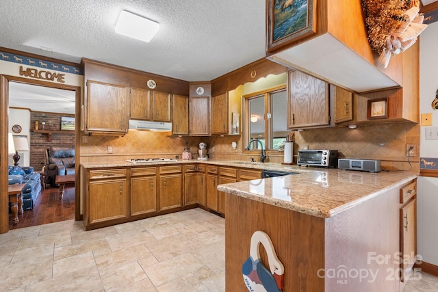kitchen featuring brown cabinetry, white gas stovetop, a sink, decorative backsplash, and under cabinet range hood