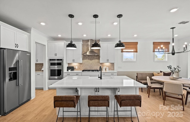 kitchen with appliances with stainless steel finishes, wall chimney range hood, a sink, a chandelier, and tasteful backsplash