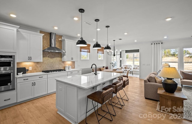 kitchen featuring wall chimney range hood, open floor plan, gas stovetop, double oven, and a breakfast bar area