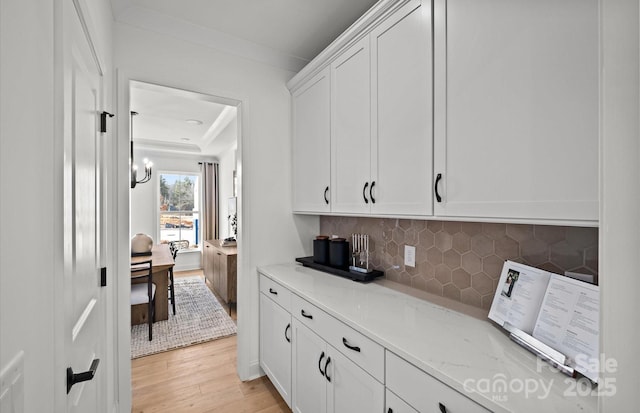 kitchen featuring tasteful backsplash, light stone countertops, light wood-style floors, and white cabinetry