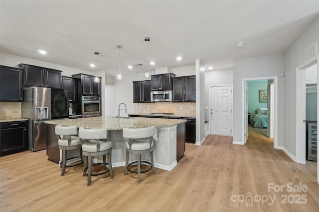 5812 Dinsmore Ln, Belmont, NC 28012 - kitchen featuring appliances with stainless steel finishes, tasteful backsplash, light stone countertops, light wood-style floors, and a center island with sink