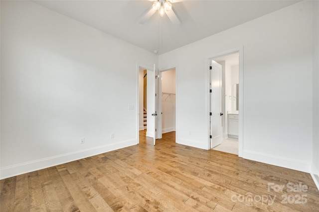 unfurnished bedroom with a spacious closet, light wood-type flooring, baseboards, and ensuite bath