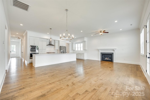 unfurnished living room with ceiling fan, a fireplace, light wood-style floors, recessed lighting, and a chandelier