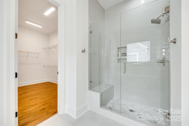 bathroom featuring a shower stall, a walk in closet, baseboards, and wood finished floors