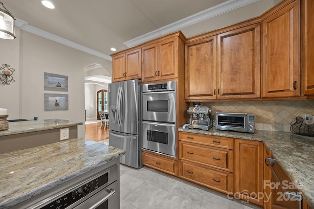 104 Golden Bell Ct, Mooresville, NC 28117 - kitchen featuring appliances with stainless steel finishes, arched walkways, crown molding, brown cabinets, and light stone counters