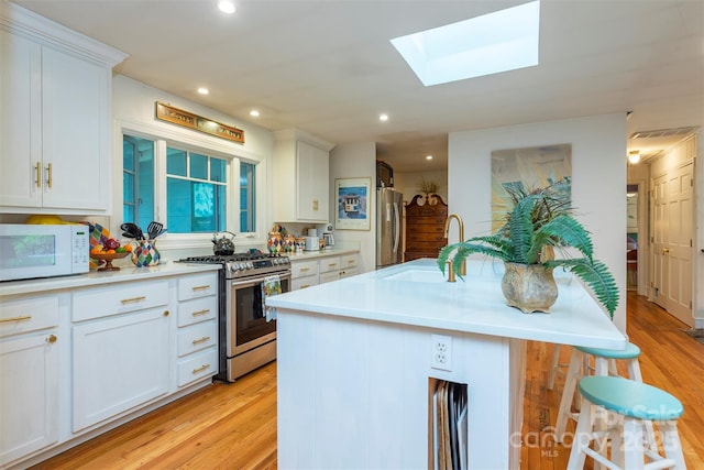 212 Vance Ave, Black Mountain, NC 28711 - kitchen with stainless steel appliances, a sink, a skylight, light wood-type flooring, and white cabinets