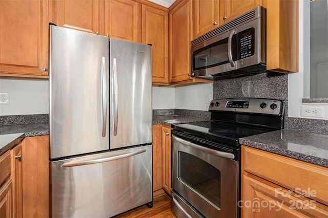 kitchen featuring stainless steel appliances, brown cabinets, dark stone countertops, and light wood finished floors