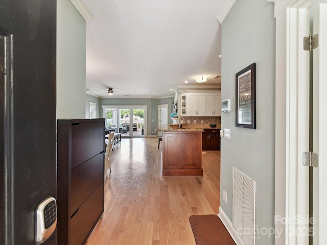 kitchen with crown molding, open floor plan, light wood finished floors, white cabinets, and decorative backsplash