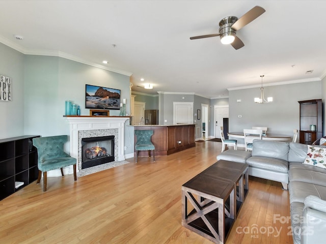 living room featuring ceiling fan, light wood-style floors, a fireplace with flush hearth, crown molding, and a chandelier