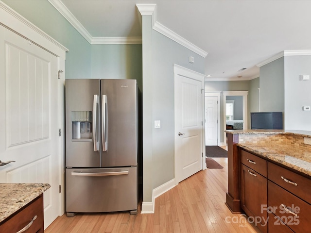 kitchen featuring stainless steel fridge, light wood-style floors, ornamental molding, light stone counters, and baseboards