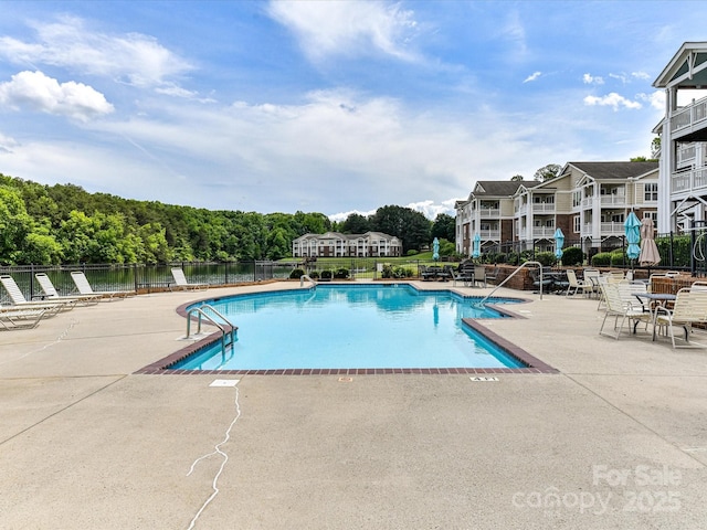 community pool featuring fence, a patio, and a water view
