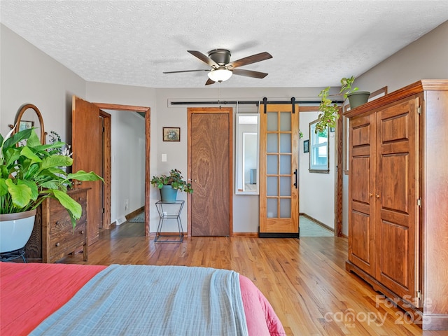 143 Mountain Crest Rd, Swannanoa, NC 28778 - bedroom featuring light wood-style floors, a barn door, baseboards, a textured ceiling, and a ceiling fan