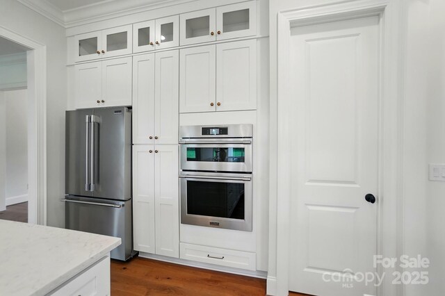 9311 Simpson Rd, Waxhaw, NC 28173 - kitchen with stainless steel appliances, ornamental molding, dark wood-type flooring, white cabinetry, and light stone counters