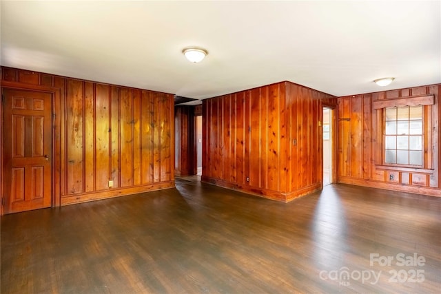 unfurnished living room featuring wood walls, wood finished floors, and baseboards