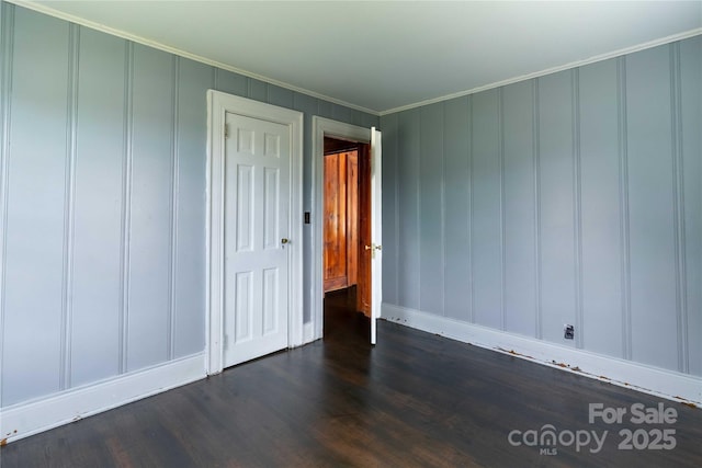 unfurnished bedroom with a decorative wall, crown molding, dark wood-style floors, a closet, and baseboards
