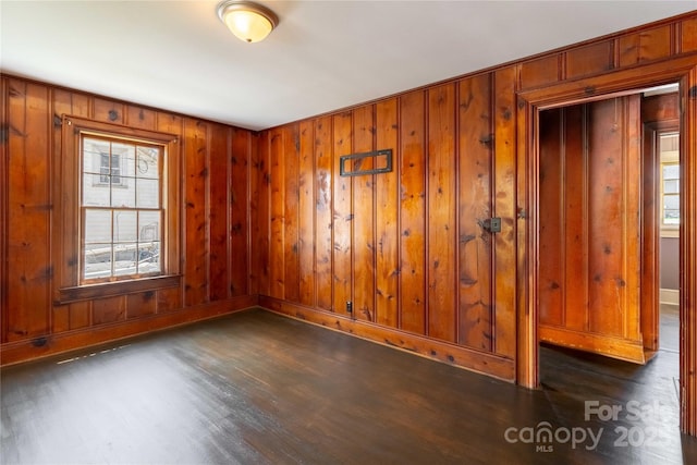 unfurnished room with dark wood finished floors, baseboards, and wooden walls