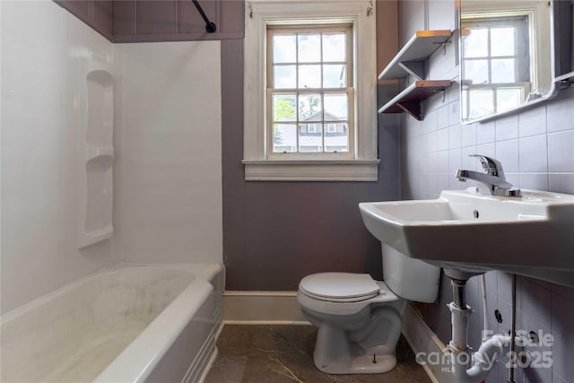bathroom with toilet, plenty of natural light, marble look tiles, washtub / shower combination, and tile walls