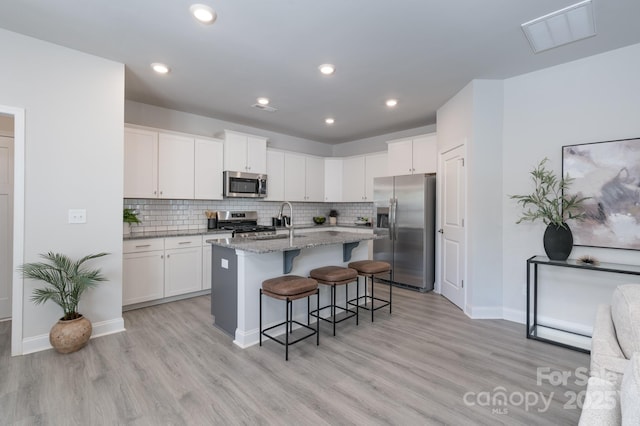 4045 Port Richmond Ave Unit 10, Gastonia, NC 28056 - kitchen featuring appliances with stainless steel finishes, a breakfast bar, light stone counters, light wood-style flooring, and white cabinetry