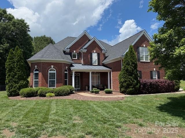 traditional home featuring brick siding, a front yard, and a porch