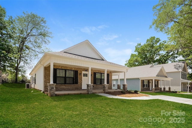 view of front facade with a porch, central AC, a front yard, brick siding, and a shingled roof