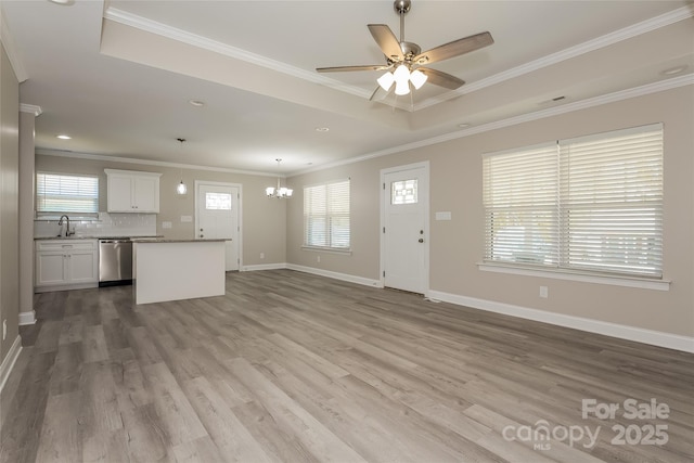 unfurnished living room featuring a sink, plenty of natural light, a chandelier, ceiling fan, and crown molding