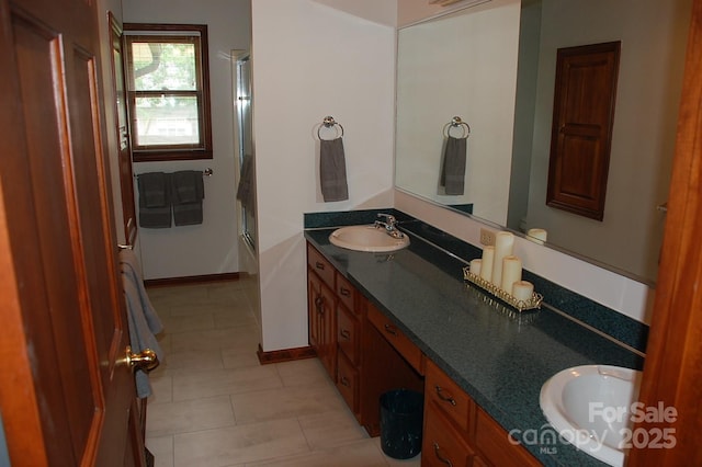 full bathroom with double vanity, tile patterned floors, baseboards, and a shower