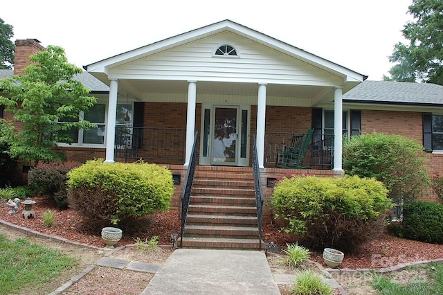 view of front facade featuring brick siding, a porch, a shingled roof, and a chimney