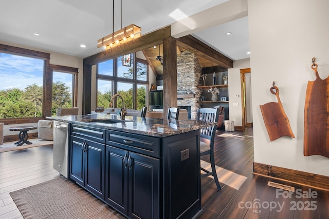 kitchen featuring a sink, dark wood-type flooring, a kitchen bar, a center island with sink, and dark stone countertops