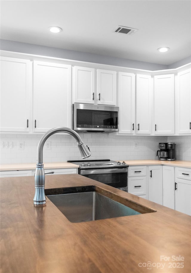 kitchen featuring stainless steel microwave, white cabinets, decorative backsplash, recessed lighting, and a sink