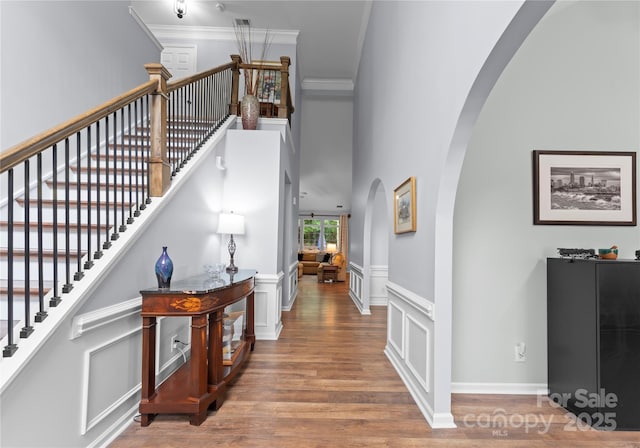 staircase featuring arched walkways, crown molding, wood finished floors, a wainscoted wall, and a decorative wall