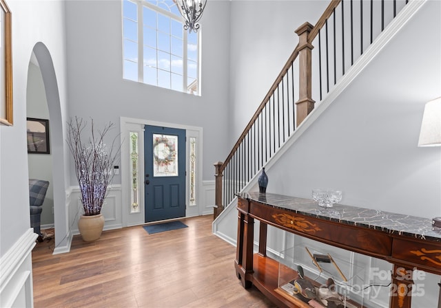 entrance foyer featuring wood finished floors, a towering ceiling, wainscoting, a decorative wall, and a chandelier