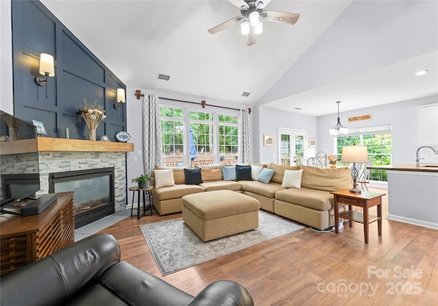 living area with a fireplace, light wood-style flooring, ceiling fan, healthy amount of natural light, and high vaulted ceiling