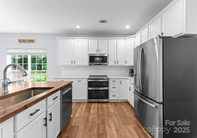 kitchen featuring appliances with stainless steel finishes, a sink, light wood-style flooring, white cabinets, and recessed lighting