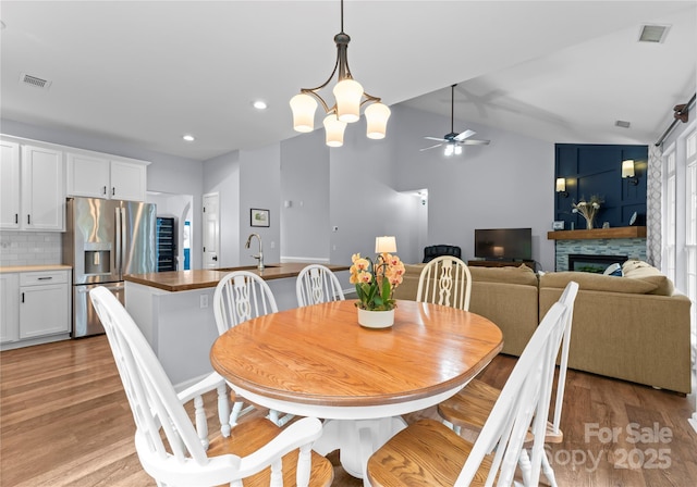 dining room featuring a ceiling fan, light wood-style flooring, a fireplace, vaulted ceiling, and recessed lighting